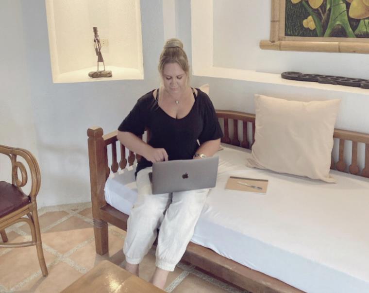 Blonde girl in black top sitting on sofa with laptop