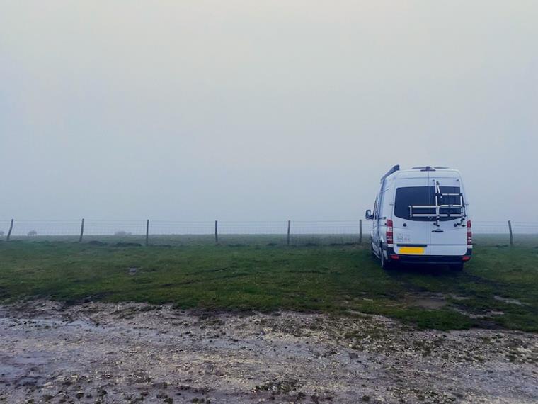White campervan parked in field in fog