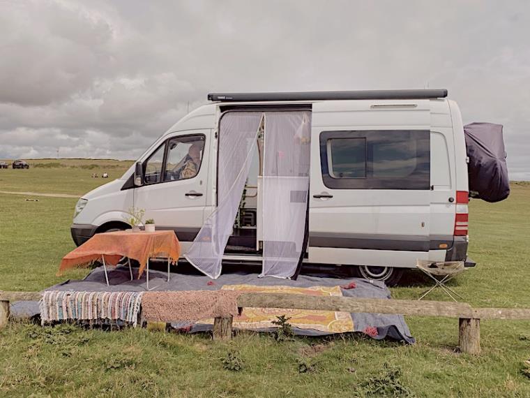 White campervan, door open rugs on grass