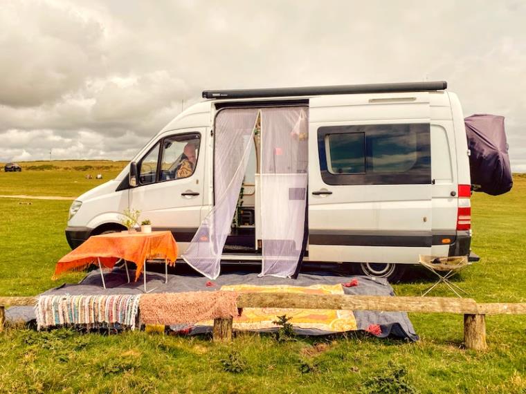 White campervan in field with door open and rugs outside