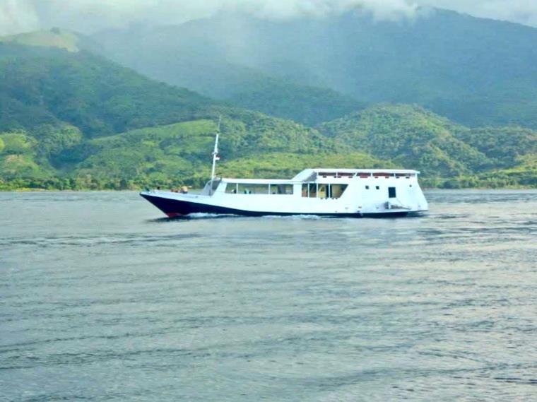 White powerboat on green sea surrounded by green hills