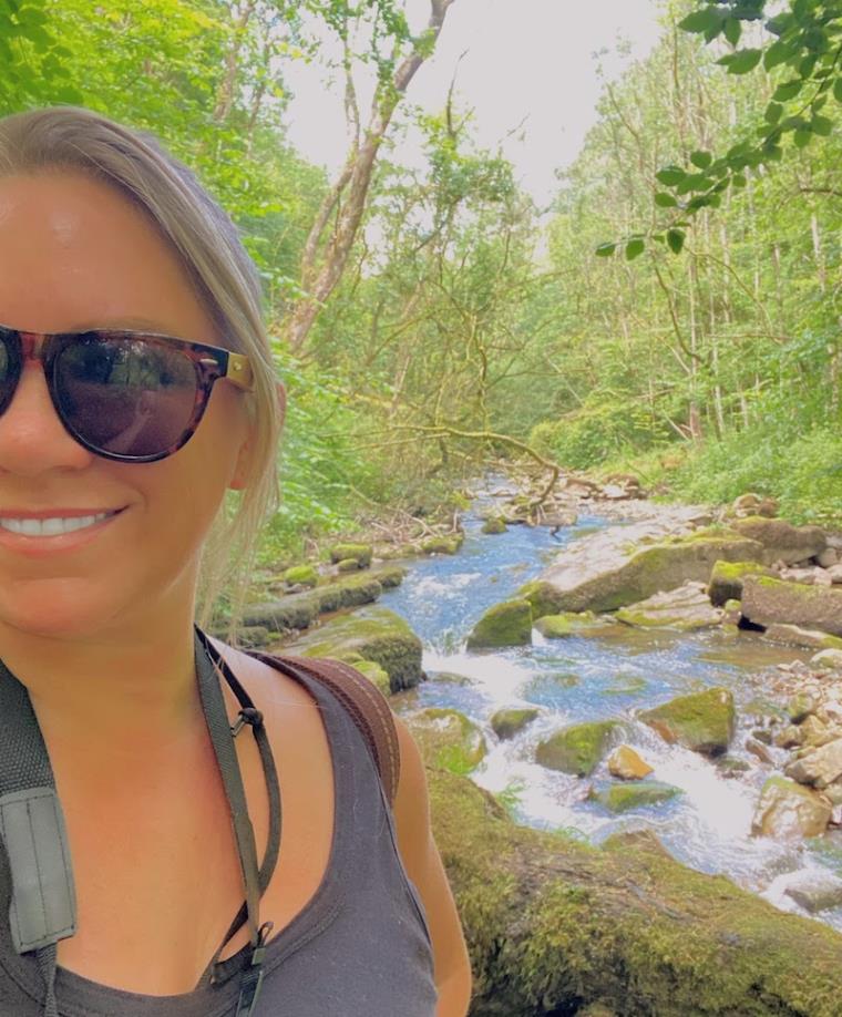 Blonde girl smiling and wearing sunglasses by a river