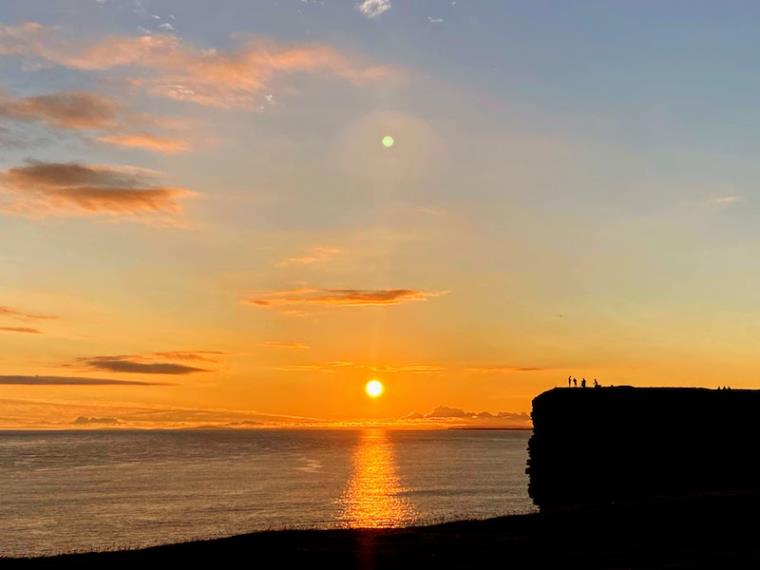 Sunset over the ocean by a silhouetted clifftop